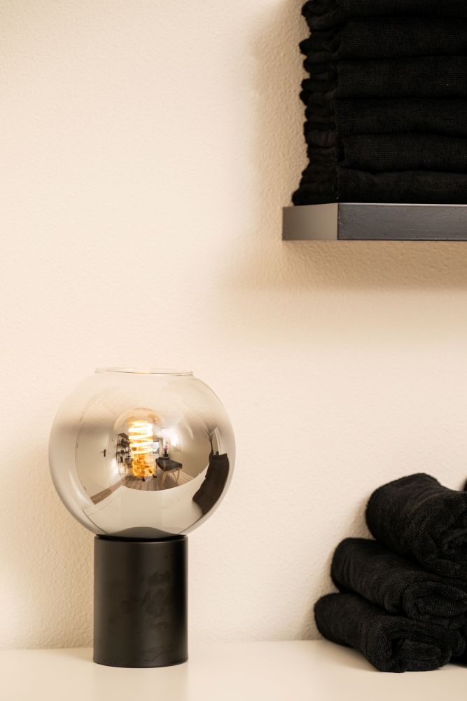 Rookglazen sfeerlamp met zwarte handdoeken op een plank in de massageruimte
